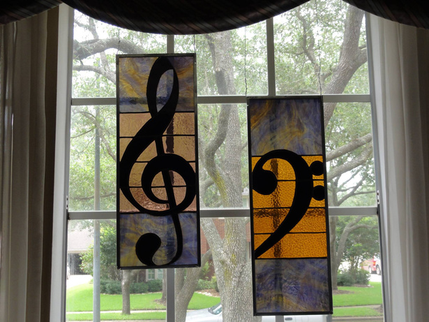 Two stained glass panels with a treble clef and bass clef hanging in a window.