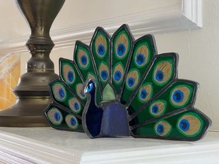 Three-dimensional stained glass peacock sculpture with a fanned tail.